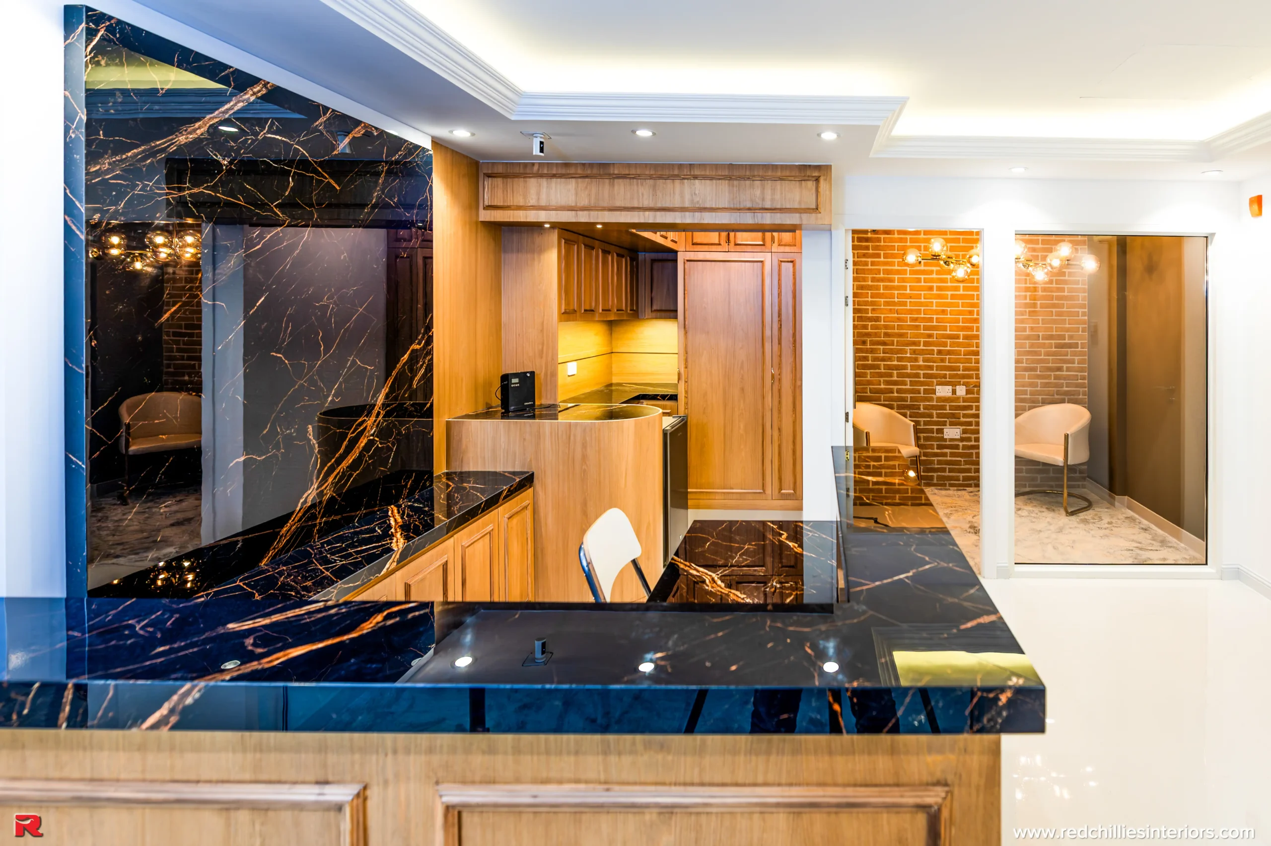 Office reception and pantry with black marble, wooden cabinetry, and exposed brick walls by RCI Red Chillies Interiors LLC.