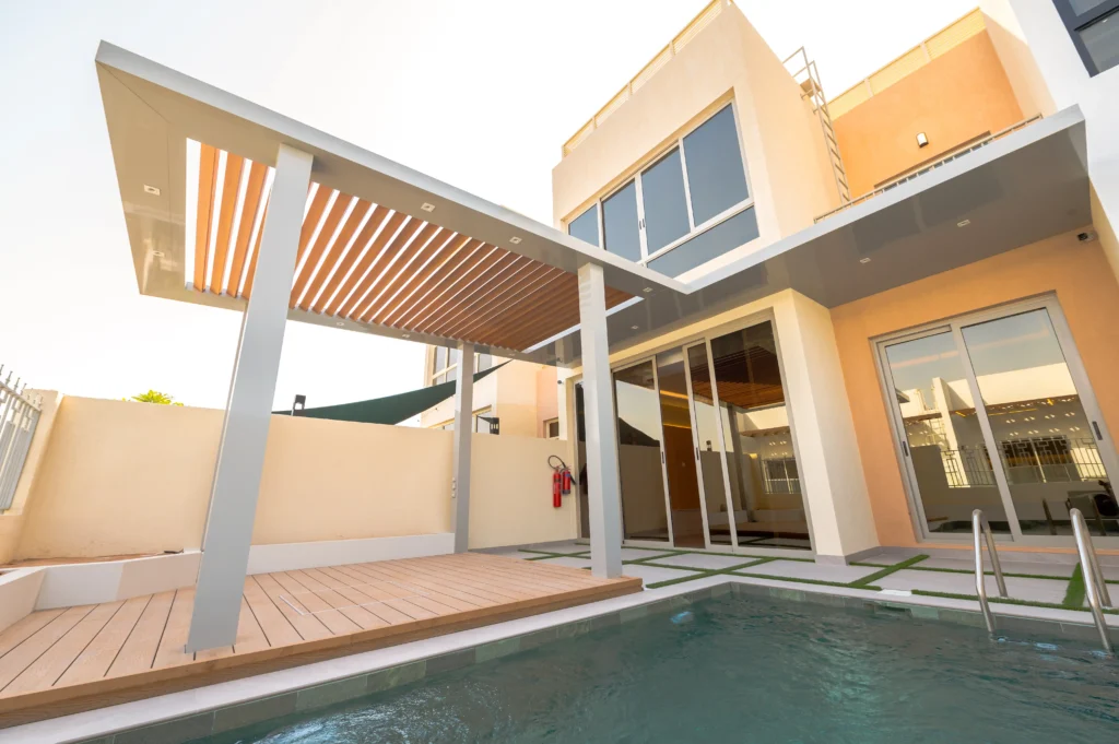 Modern patio with a pergola and adjacent swimming pool at a villa in Al Furjanby by RCi-Red Chillies Interiors